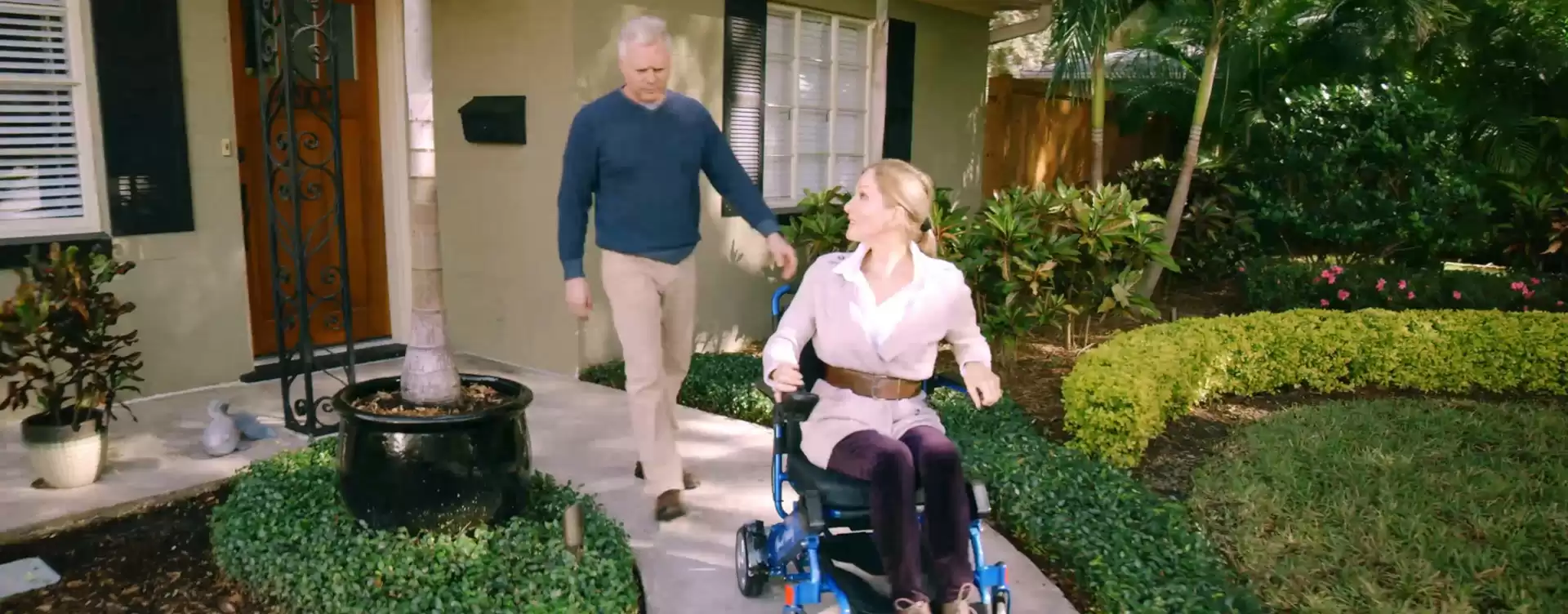 A man and woman in an electric wheelchair in front of a house.