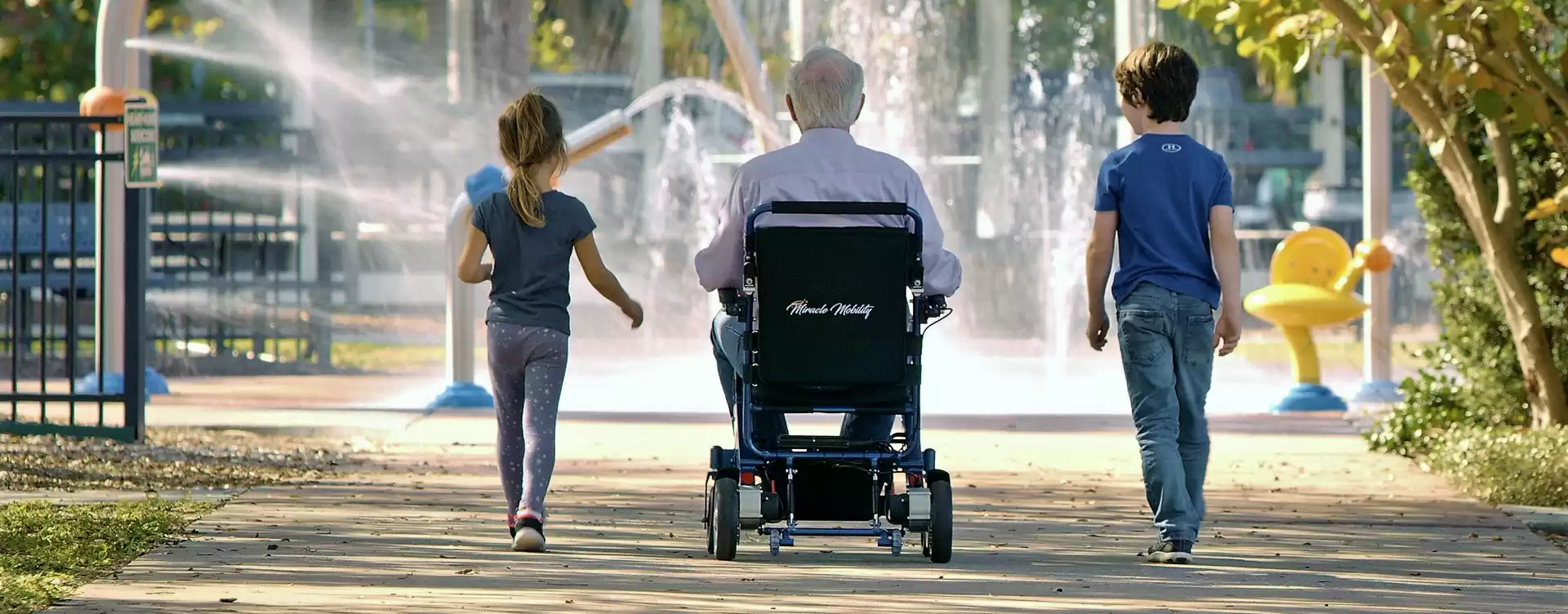 A man in an electric wheelchair and two children walking down a path.